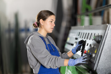 Girl workshop employee switches toggle switch on control panel, supervises production process using control panel. Employee works at center control panel.