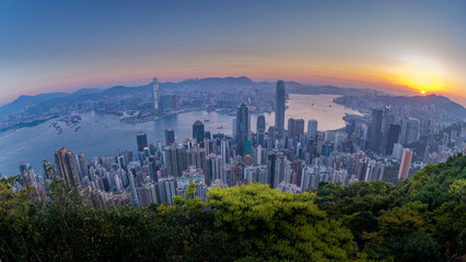 HongKong skyline at sunrise over harbor, wide panoramic city view with glowing sun and morning haze
