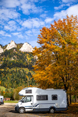 Motorhome camper van parked under autumn tree with mountain landscape