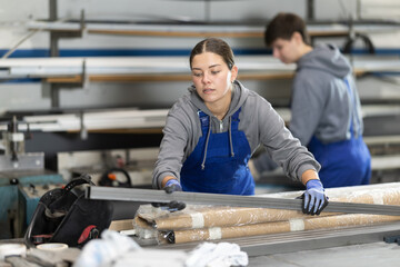 Young woman worker in uniform taking steel profile pipe in warehouse