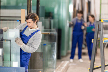 Man glazer employee in blue overall works in glass processing shop. He carries out installation work, products for renovation of residential premises made of glass and plastic..