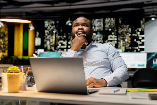African american guy at the workspace sitting in deep concentration, pondering for a decision. Using laptop as he applies rational thinking and intuition for issue, mental haze.