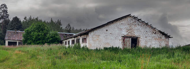 Panorama of large abandoned farm building with damaged windows and roof. High value of running agriculture business. Old worn out barn. Rising price and troubled economy effect on running a ranch