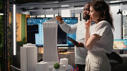 Property developers discuss the challenges of city planning and land acquisition, using 3D models to visualize residential layout expansion and infrastructure upgrades on the table.