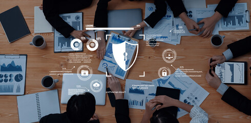 A diverse team collaborates around a wooden table, discussing data analysis and cybersecurity, with charts and laptops highlighting modern office dynamics and teamwork. Trope