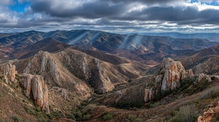 Rugged mountain landscape reveals dramatic sunbeams piercing through dark cloud cover