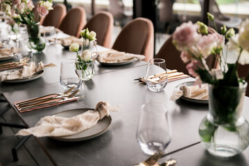 Close-up of a styled dining table featuring gold cutlery, neutral linens, glassware, and delicate...