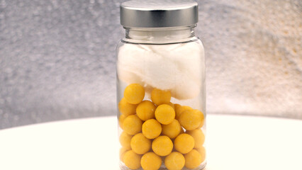 Yellow vitamins in a clear glass bottle with cotton.