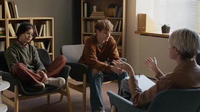 Female therapist leading two teenagers toward reconciliation during couple therapy session in counseling office when partners holding hands after conflict resolution