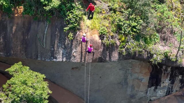 Close-up drone shot of two women abseiling down a rock in Minas Gerais, Brazil