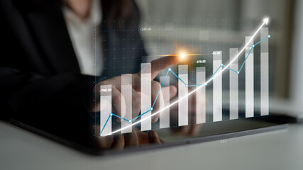 A business professional interacts with a digital tablet displaying a financial growth chart. The rising graph symbolizes success and modern analytics in a corporate environment. Impute