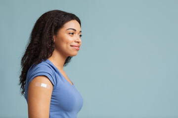 After vaccination concept. Happy black lady with adhesive bandage on arm after covid-19 vaccine...