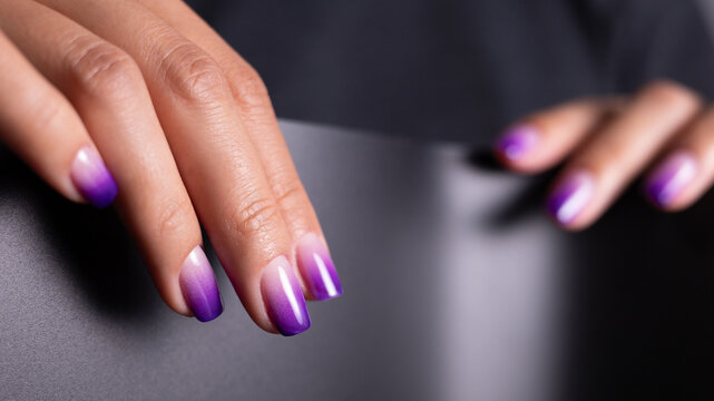 Professional purple ombre manicure on woman hands. Stylish nail art, cosmetics and self care concept on dark background.