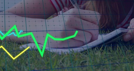 Writing woman striped shirt lying on grass, using pen on spiral-notebook, neon line graphs and grid