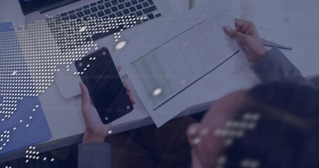 Holding black smartphone, woman wearing gray suit checking table at white desk with laptop LED dots