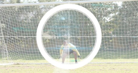 Crouching keeper wearing yellow jersey, gloves guarding soccer goal net at soccer field lens flare © vectorfusionart