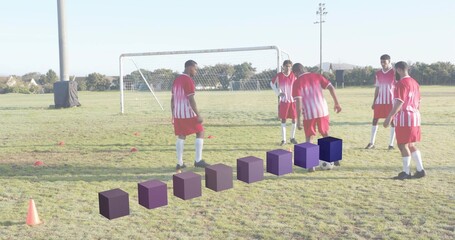 Practicing five male players passing soccer ball on grass pitch in red-and-white jerseys near goal