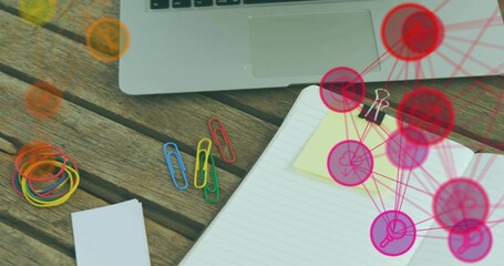 Showing open notebook with yellow note clipped by clip sitting at desk, laptop and pink or red overl