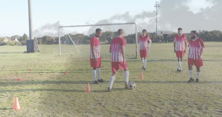 Dribbling five men in red-and-white jerseys controlling soccer ball on community field, with cones