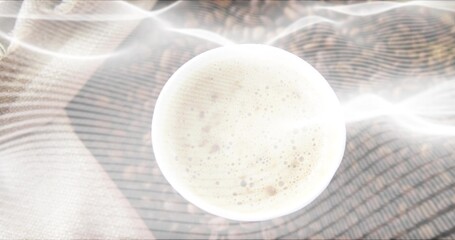 Presenting white ceramic cup sitting on woven textile, showing frothy coffee, crema, light streaks