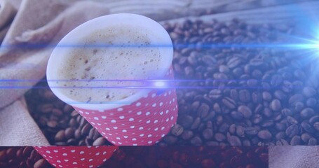 Showing red polka-dot cup containing frothed coffee on table with burlap and beans, blue lens flare