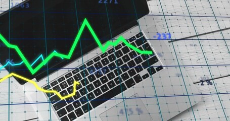 Displaying silver laptop keyboard and trackpad on gridded papers at desk, showing blue grid charts