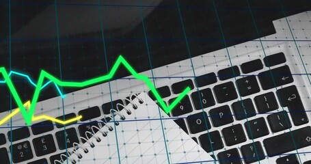 Displaying laptop keyboard with spiral notebook at workstation, with blue grid and neon graphs
