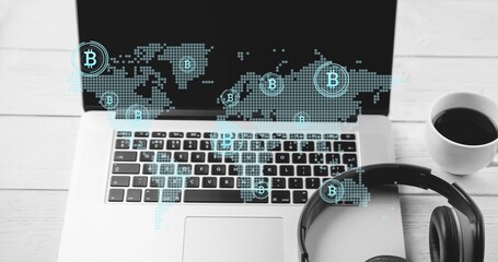 Projecting silver laptop showing dotted map and Bitcoin icons on home desk, with headphones, coffee