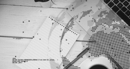 Showing spiral notepad resting diagonal on wood desk with pen, keyboard, coffee, halftone map, code