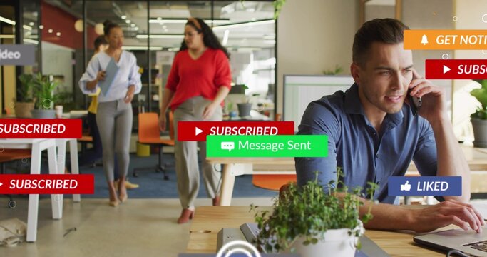 Talking man in blue shirt using laptop and headset at open-plan office desk, with overlay graphics - Powered by Adobe