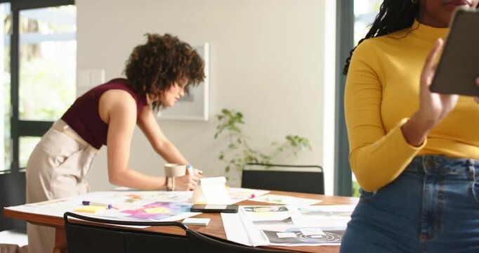 Tablet content guiding diverse female colleagues scrolling and sketching designs on work table