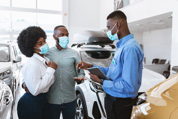 Black couple in face masks buying new auto during covid lockdown, taking car key from salesman at automobile dealership. African American family purchasing or renting new vehicle at showroom