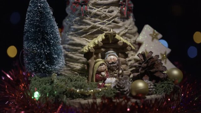 Close-up of a creative mini Christmas tree made of rope with nativity scene, rotating on black background and blurred colorful light