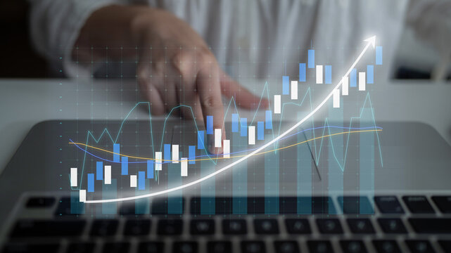 A person analyzing financial data on a laptop, featuring a digital graph overlay that depicts investment trends and market insights in a modern workspace. Impute - Powered by Adobe