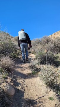 Hiker with backpack and tripod hiking up a desert dirt trail