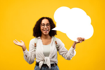 A person with curly hair stands against a bright yellow background. She smiles and gestures with one hand while holding a speech bubble in the other hand. This scene shows a friendly moment.