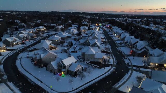 Drone flight over snowy residential area with snow-covered residential homes at oft snowfall in winter. Sunset time at dusk. Flyover shot. New development housing area of american town. Wide shot.