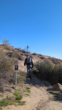 Hiker with backpack tripod hiking up a desert trail hill. Copy space.