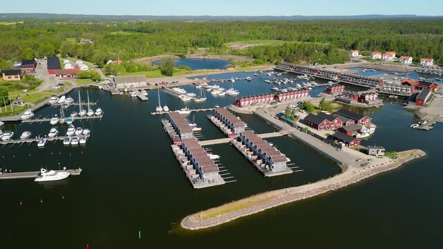 Drone flying forward towards Sunnan&aring; Hamn harbor with a slow tilt down revealing colorful fishing huts, boat docks, and the blue waters of Lake V&auml;nern in Mellerud Sweden during summer