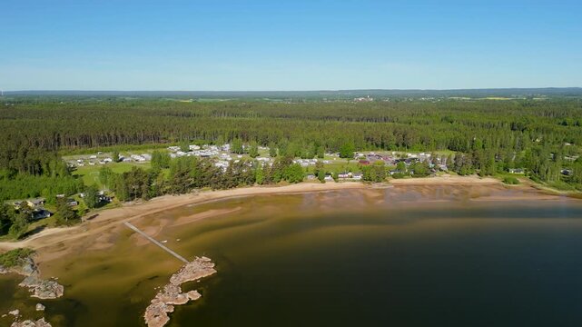 Dramatic aerial pull back shot starting from the wooden pier revealing the long sandy shoreline of Vita Sandar Beach and the nearby camping resort on Lake V&auml;nern in Mellerud Sweden during summer