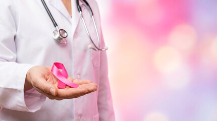 Doctor holds pink ribbon in hand during awareness event for breast cancer on pink warm background focused on education and support for patients and families