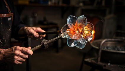 Crafting a glass flower in a hot shop where skilled artisans shape molten glass with tools during the glassblowing process at a busy workshop
