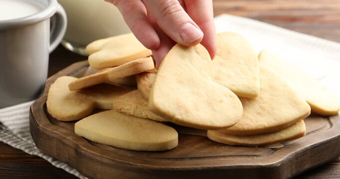 Woman taking tasty heart shaped butter cookie from board at wooden table, closeup