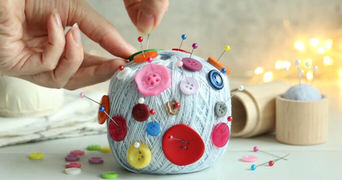 Woman sticking pin and button into skein of yarn at white table, closeup