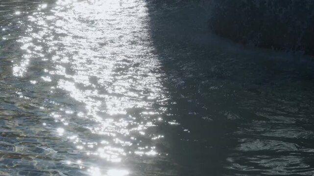 太陽の光　強い朝の日差しを反射してキラキラ光る公園の噴水池の水　波打つ波紋とみずしぶき　
