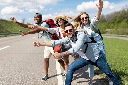 Cheerful young people standing on roadside, stopping car, trying to get free ride, having autostop journey, free space. Exciting travel adventure, hitchhiking with friends, summer holidays concept