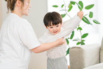 A mother helps her son get dressed in the living room at home
