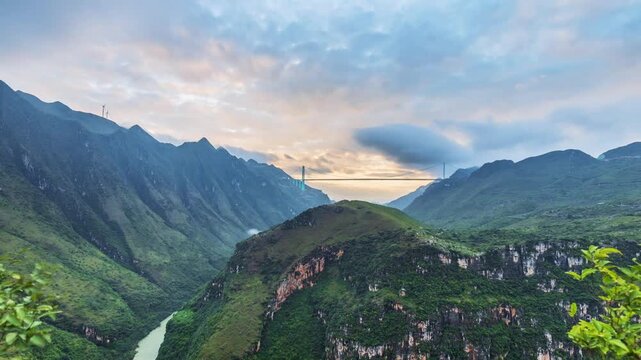 Sunrise time-lapse over a majestic suspension bridge spanning a deep canyon,with golden light illuminating mountain peaks and flowing river below, Huajiang Canyon Bridge in Guizhou Province, China