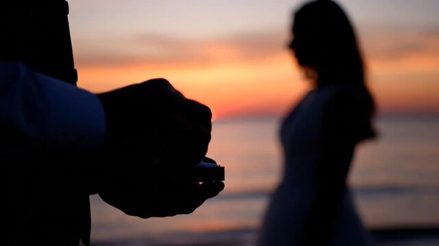 Cinematic silhouette of a man proposing with an engagement ring to a woman on a beach at sunset
