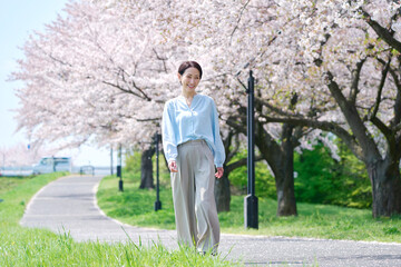 満開の桜と遊歩道を歩く女性
